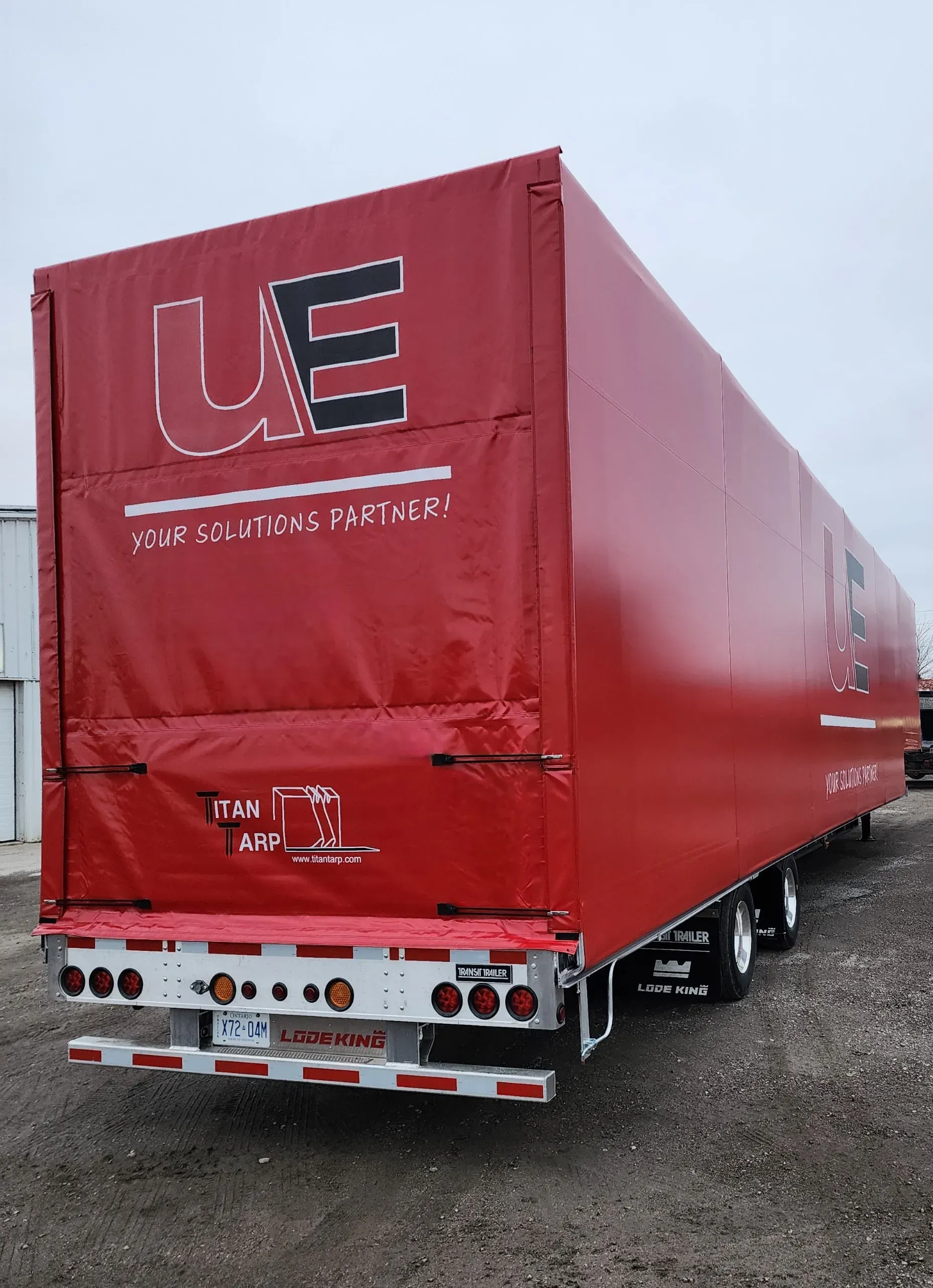 A transport truck trailer with a red tarp and Titan Tarp branding