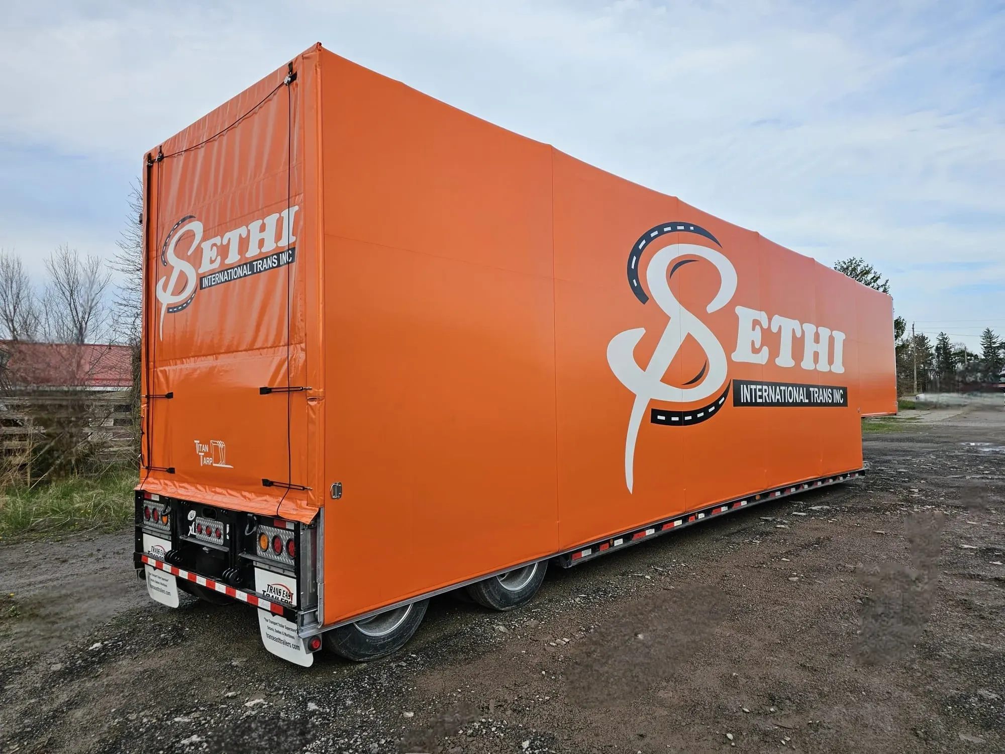 A double drop deck trailer with an orange Titan tarp system, seen from the rear