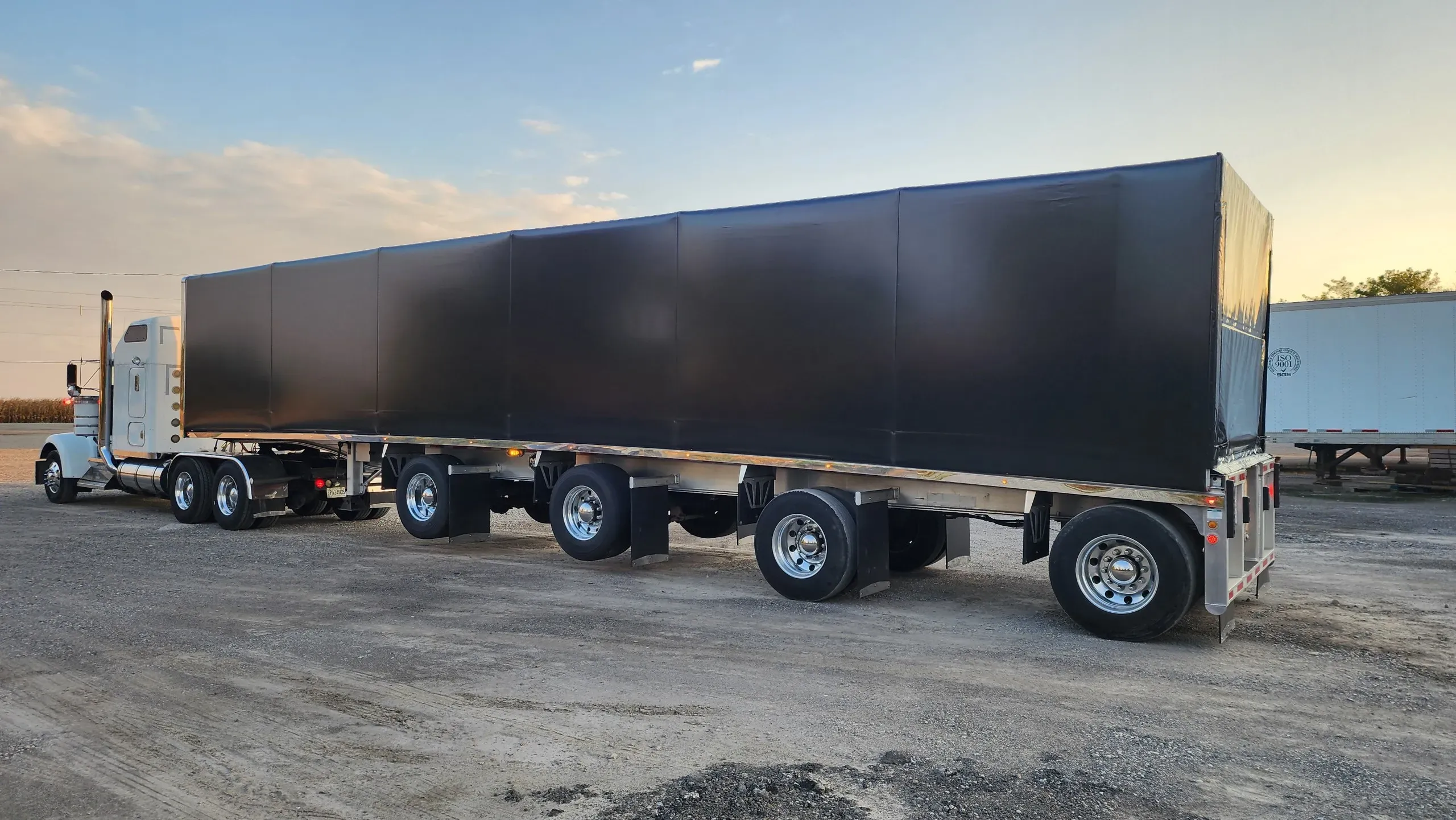 A flatbed trailer with a black Titan sliding tarp system, seen from the side