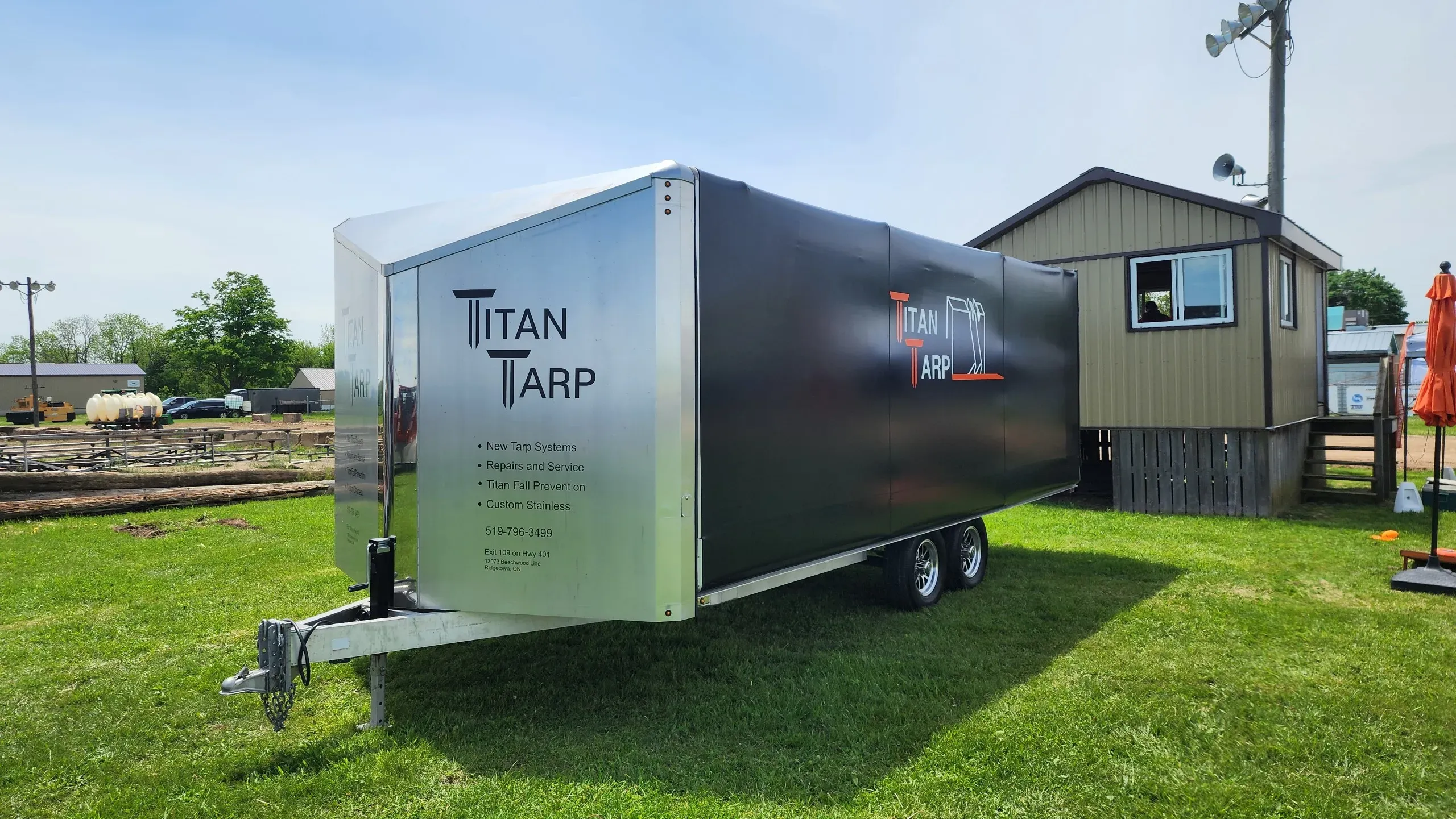 A utility trailer with a Titan tarp system and stainless front, parked on grass